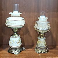 Pair of floral painted hurricane table lamps, one with brass base, both with glass chimneys and ruffled collars.