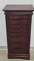 Front view of closed jewelry armoire with 8 visible drawers and decorative molding at top and base