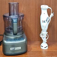 Food processor visible with food processing bowl, feed tube, and control buttons. Kalorik immersion blender placed next to it with power cord.