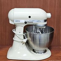 Front side view of the off-white KitchenAid tilt-head stand mixer with stainless steel bowl and attachments inside bowl.