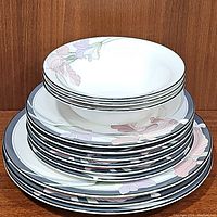 Stack showing three bowls on top of six dessert plates and three dinner plates all with matching floral black rim design.