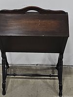 Closed view of vintage standing wooden sewing box showing dark wood finish and scalloped carry handle.