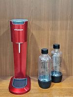 Red SodaStream G100 sparkling water maker machine with tray and two clear carbonating bottles with black caps and bases.