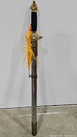 Full length view of the Tai Chi sword in its metal scabbard showing the lion head guard, decorative tassel, black wrapped handle, and metal pommel with tassel attachment.