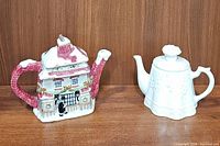 Two teapots displayed side by side on a wooden shelf, showing overall front view.