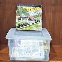 Photo showing the HO scale Atlas Trains 'Over N' Under Pier Set' box resting on a clear container holding assorted train track pieces.