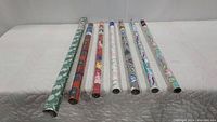 7 rolls of wrapping paper laid out horizontally showing various colorful designs.