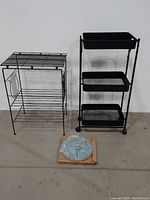 Photo showing all three items together: black wire plant stand, 3-tier metal mesh cart, ceramic sundial on cardboard box
