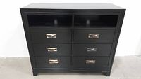 Full front view showing ebony finish chest with two open storage compartments on top and six drawers below with metal pulls.