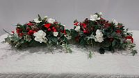 Two Christmas flower arrangements side by side on a white quilted surface, showing size and shape.