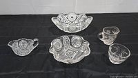 Set of three glass bowls including two centerpiece bowls and one creamer and sugar bowl set arranged on black background.