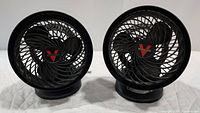 Two black Vornado desk fans side by side on a white surface, front view showing blades and logo.