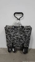 Foldable utility cart in its collapsed and folded form, with camouflage fabric and handle wrapped in plastic