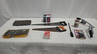 Photo showing an assortment of hand tools including tap and die set, two hand saws, large screwdriver, glass jar with hardware, Lo Back Trax and other hardware.