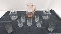 Grouped photo of entire glass set on black background showing pitcher, candy dishes, and etched glasses