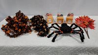 Photo showing two pumpkin face garlands, black and orange spider decoration, three small orange Halloween hangable decoration boxes, and a bunch of orange artificial leaves set on white background.