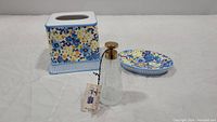 Three items: ceramic tissue box cover, matching soap dish, and glass atomizer with brass top all placed on white surface