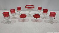 Front view showing the full set of red glassware including the pedestal bowl at center, surrounding crown-style glasses, and two ruffled rose bowls in front.