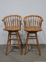 Front view of two vintage MCM Windsor style solid wood swivel bar stools placed side by side.