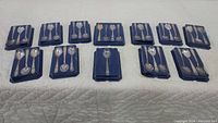 Wide view of multiple sets of Wm Rogers silver plated collectible spoons in blue velvet presentation boxes, showcasing several pairs and sets arranged in rows on a white surface.