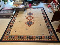 Full top view photo of the rectangular beige Korhani carpet showing central diamond patterns and border design with animal motifs, placed in a room with furniture around.