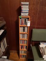 Front view showing 7-shelf narrow wooden stand filled with CDs and additional CDs stacked on top.