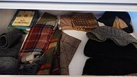 Photo showing folded scarves with wool and alpaca textures, several in plaid and pattern designs in various colors.