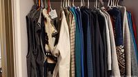 Hanging men's clothing items including vests, sweaters, and shirts showing variety of colors and materials