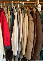 Various men's jackets and coats on hangers, showing different colors and styles including a red puffer and several leather coats.