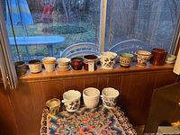 Wide view of more than a dozen small planters arranged on windowsill and table, showing variety in styles and colors