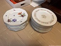 Top-down view of 10 octagonal Rosenthal plates and 12 round Premiere china plates stacked in two groups on the floor.