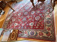 Full view of rectangular red floral area rug under table on hardwood floor