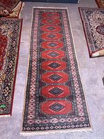 Full view of the handwoven wool runner rug showing the full pattern and colors on concrete floor alongside other rugs.