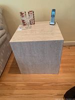 Stone side table placed on hardwood floor next to couch, showing square shape and stone texture.