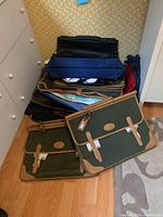 Stack of various tote bags including green canvas tote bags with tan trim and buckle closures, black briefcase style tote, navy blue bags.