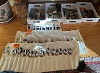 Flatware set displayed with knives, forks, and spoons in rolled cloth holders and white trays on table.