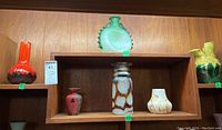 Shelf displaying seven diverse pottery and glass vases in different styles and colors.