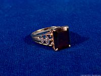 Triangular side view showing filigree shoulders, evil eye motifs with diamond accents, and prong-set rectangular garnet.