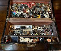 Full view of open wooden box with assorted jewelry pieces inside, showing contents in top and lower compartments.