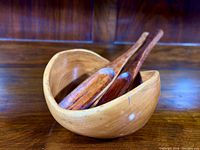 Front view of the cedar salad bowl with the two wooden salad tools inside, showing the bowl's smooth light wood finish and curved shape.