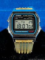Front of Casio digital watch showing time, day, date, and function labels with gold tone bracelet.