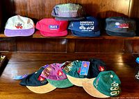 Display of 8 vintage hats on wooden surfaces showing front and visor details. Hats include branded logos from McDonald's 1996 Olympics, The New VR, Hatz Diesel, Donegan's Haulage, and ES XD3 Extra.