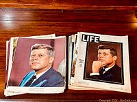 Stack of vintage magazines featuring John F. Kennedy on the covers, arranged on wooden surface.