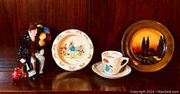 Photo showing the Balloon Man figurine, Bunnykins golf bowl, Bunnykins cup and saucer, and series ware plate arranged side by side on shelf.