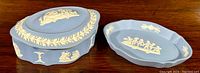 Photo showing both the Wedgwood jasperware lidded trinket box and matching trinket tray side by side on a wood table.