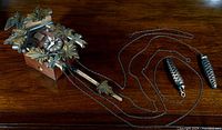 Full view of carved wooden clock case, chains and two pinecone weights laid out on table