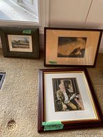 Three framed prints displayed on beige carpet near window, various sizes and frames.