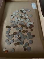 Overview of the mixed coins spread inside a cardboard box, showing varying sizes and colors.