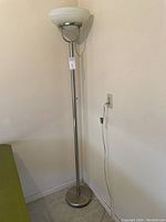 Full view of the adjustable metal floor lamp with frosted glass bowl shade next to a wall outlet.