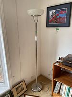 Full view of adjustable metal floor lamp standing in corner with a white bowl-shaped glass shade at top, and power cord trailing to wall socket.